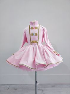 a pink dress with gold trimmings and buttons on the collar is sitting on a metal stand