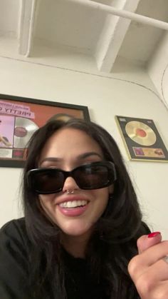 a woman wearing sunglasses is smiling and holding something in her hand while sitting at a table