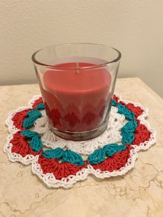 a red candle sitting on top of a table next to a crocheted doily