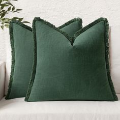 two green pillows sitting on top of a white couch next to a potted plant