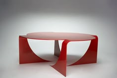 a red table sitting on top of a white floor next to a gray wall in an empty room