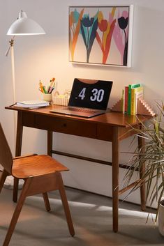 a wooden desk topped with a laptop computer sitting next to a chair and potted plant