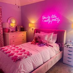 a bed with pink sheets and pillows in a room that has lights on the wall