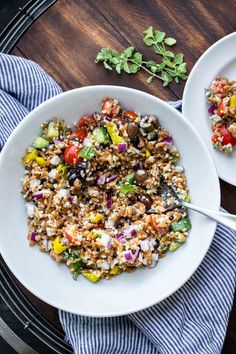 two white bowls filled with colorful salad on top of a wooden table next to a blue and white towel