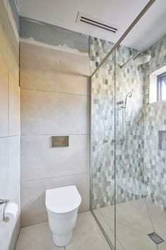 a white toilet sitting in a bathroom next to a walk in shower and tiled walls