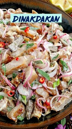 a bowl filled with meat and onions on top of a table next to lemon wedges