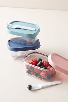 two plastic containers with berries and blueberries in them on a white counter top next to spoons