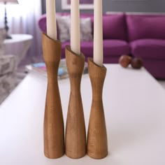 three wooden candlesticks sitting on top of a white table next to a purple couch