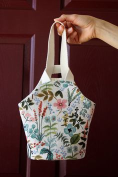 a hand holding a white bag with flowers on it and a red door in the background