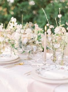 the table is set with white and pink flowers, wine glasses, candles and plates