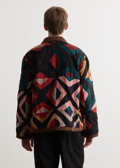 a young boy standing in front of a white wall wearing a jacket with geometric designs on it