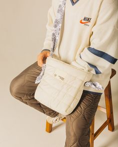 a man sitting on a chair holding a white purse with an orange nike logo on it