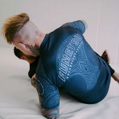 a man with tattoos on his arm and leg in a blue shirt laying on top of a bed