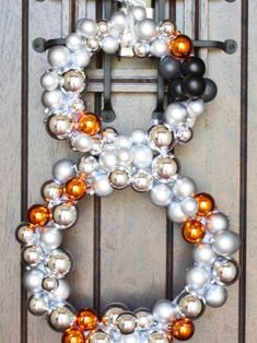 a wreath made out of silver and orange ornaments hanging on a wooden door with hooks