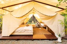 a bed sitting inside of a tent on top of a wooden platform next to trees