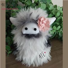 a stuffed animal with a pink flower on its head sitting next to some green plants