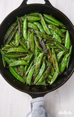 a skillet filled with green beans on top of a white table next to a cloth