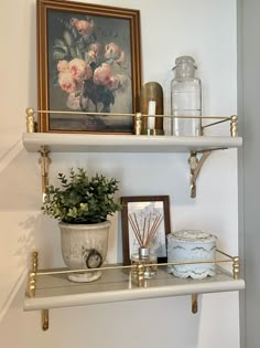 a shelf with flowers and candles on it in a room next to a framed painting