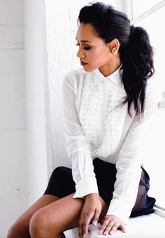 a woman sitting on top of a white chair in front of a window with her legs crossed