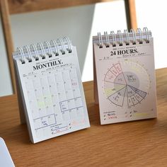 two calendars sitting next to each other on a wooden table with a computer mouse