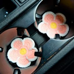 two crocheted flowers sitting in the center console of a car, one is pink