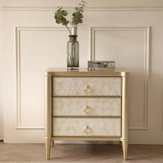 a white and gold chest of drawers with flowers in a vase sitting on top of it