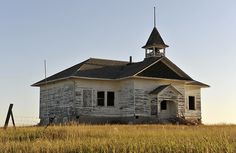 an old white church with a steeple in the middle of a grassy field at sunset