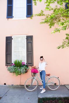 a woman standing next to a bicycle with flowers in the basket on the handlebars