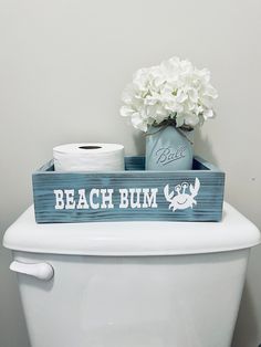 a toilet with a wooden sign that says beach bum on it and flowers in a vase