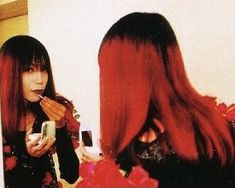 a woman with long red hair brushing her teeth in front of a mirror while looking at herself in the mirror