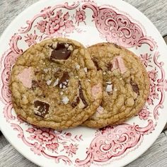 two chocolate chip cookies sitting on top of a white and pink plate with red designs