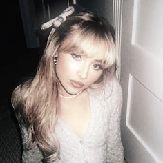 a woman with long blonde hair standing in front of a door and looking at the camera