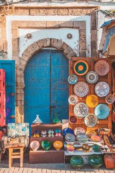 an outdoor shop with plates and bowls on the outside, in front of a blue door