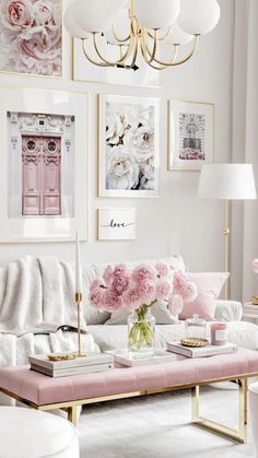 a living room filled with white furniture and pink flowers on the coffee table in front of a chandelier