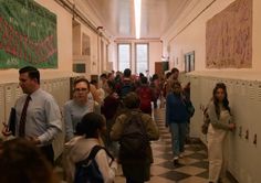 a group of people standing in a hallway next to lockers with posters on the walls