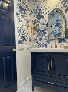 a bathroom with blue and white wallpaper, gold fixtures and a large mirror over the sink