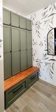 an empty room with green cabinets and wood flooring in front of a wallpapered wall