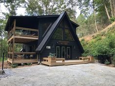 a large black cabin in the woods with stairs leading up to it's second floor