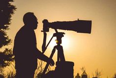 a man standing next to a camera on top of a tripod in front of the sun