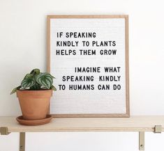 a potted plant sitting on top of a wooden shelf next to a framed sign