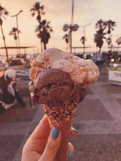 someone holding up an ice cream cone with sprinkles and chocolate frosting