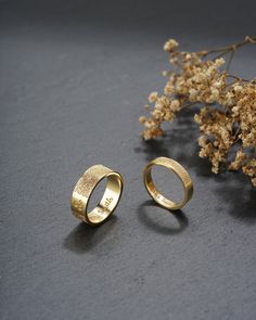 two gold wedding rings sitting next to each other on a table with flowers in the background