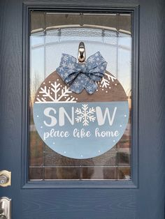 "Snow Place Like Home round wood sign topped with denim blue snowflake bow. Stained in chocolate gel and a white washed blue base. Design is complemented with white lettering and silver glitter snowflakes.  Comes ready to hang with twine to complete your front porch or a beautiful piece for inside your home! Sign measures approximately: 19 1/4\" round and 1/4\" thick for Large (pictured) 14\" round and 1/8\" thick for Small  Each sign is handmade and each wood piece is unique. Because of this wo Snowman Front Door Sign, Snowflake Wood Sign, Round Winter Door Hangers, Winter Round Door Signs, Winter Door Signs Front Porches, Winter Door Rounds, Let It Snow Round Wood Sign, Wood Round Signs Diy, Snowflake Door Hanger