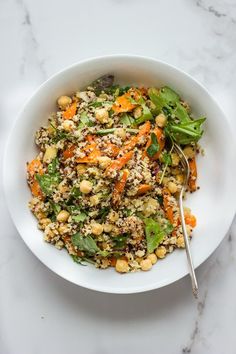 a white bowl filled with salad on top of a marble countertop next to a silver spoon