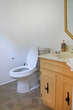 a white toilet sitting in a bathroom next to a wooden sink vanity with a mirror above it