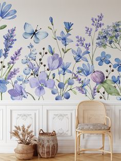 a chair sitting in front of a wall with blue flowers painted on it and a basket next to it