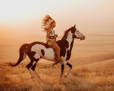 a native american man riding on the back of a brown and white horse in an open field