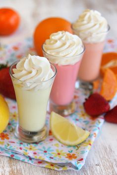 three desserts with whipped cream, lemon and strawberries on a table next to oranges