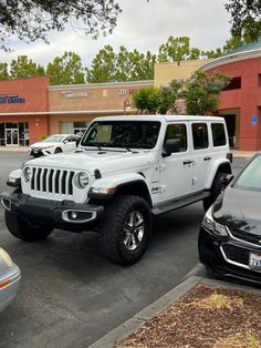 two white jeeps parked in front of a building on a parking lot next to other cars