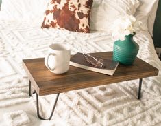 a coffee table with a book, mug and flower on it in front of a bed